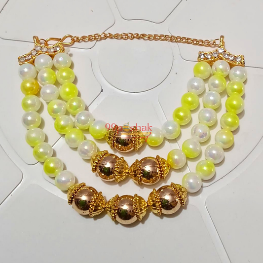 A gold-plated multi-strand pearl necklace with white and yellow-green beads, featuring ornate gold spacer beads and a rhinestone-embellished clasp, displayed on a white geometric background.