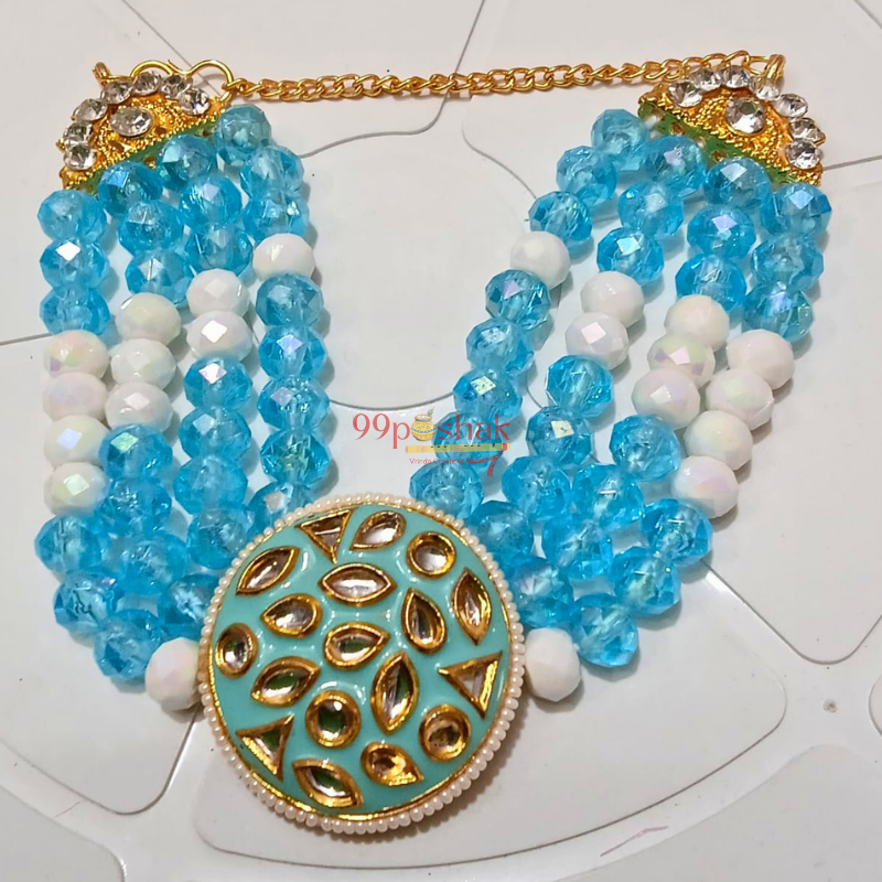 A multi-strand statement necklace featuring light blue faceted beads, white beads, a gold chain, and a large round turquoise and gold pendant with gold teardrop motifs.