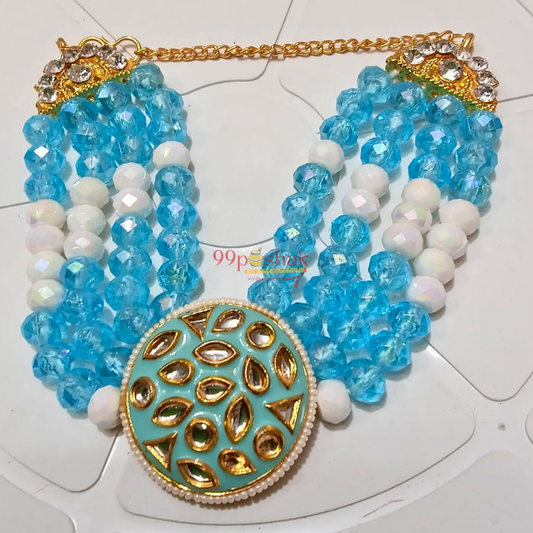 A multi-strand statement necklace featuring light blue faceted beads, white beads, a gold chain, and a large round turquoise and gold pendant with gold teardrop motifs.