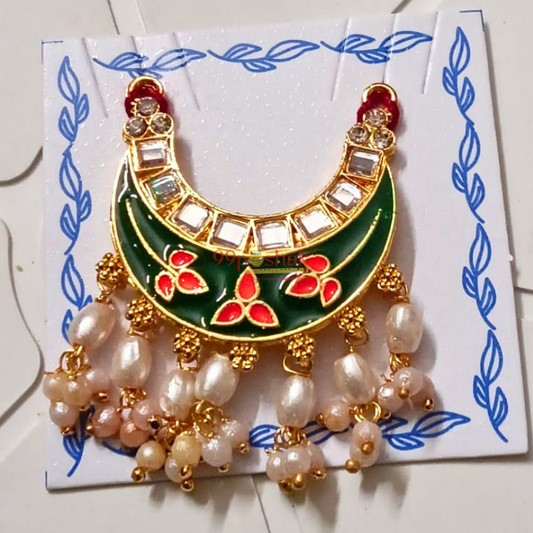 A gold crescent-shaped brooch with green enamel, red floral accents, clear rhinestones, and dangling pearl-like beads, displayed on a white card with blue leaf borders.