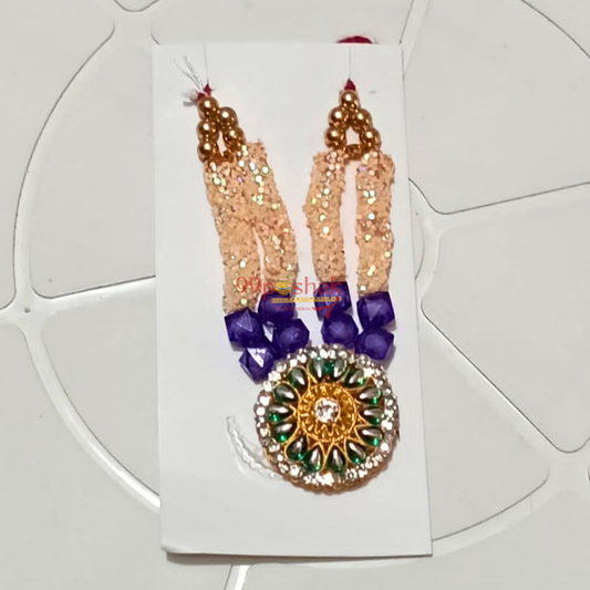 A traditional Indian bridal necklace (Jhumka) set on a white display card. The necklace features a large round gold-toned pendant decorated with green, white, and purple stones, hanging from a peach-beaded chain with purple bead accents.
